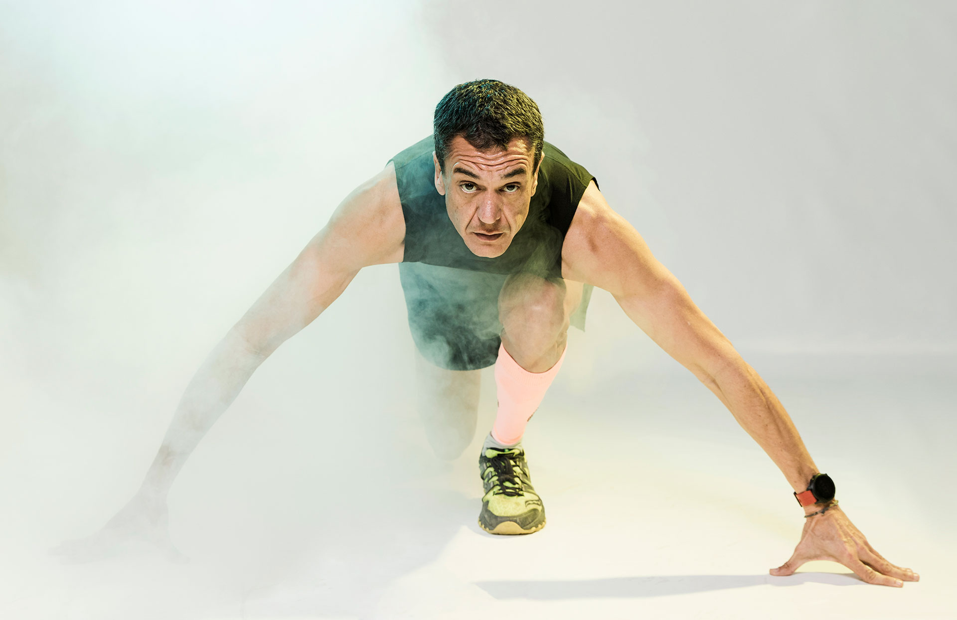 Focused male athlete in a starting position, ready for a sprint in a dramatic, fog-filled environment.
