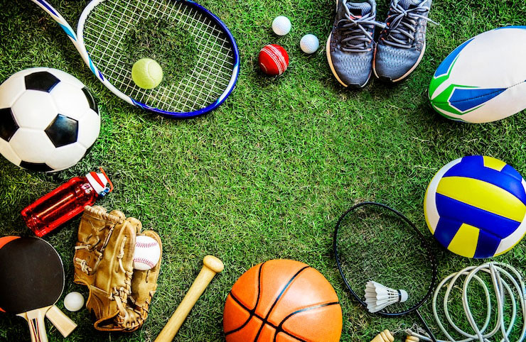 Variety of sports equipment arranged on grass, including soccer, tennis, and basketball gear.