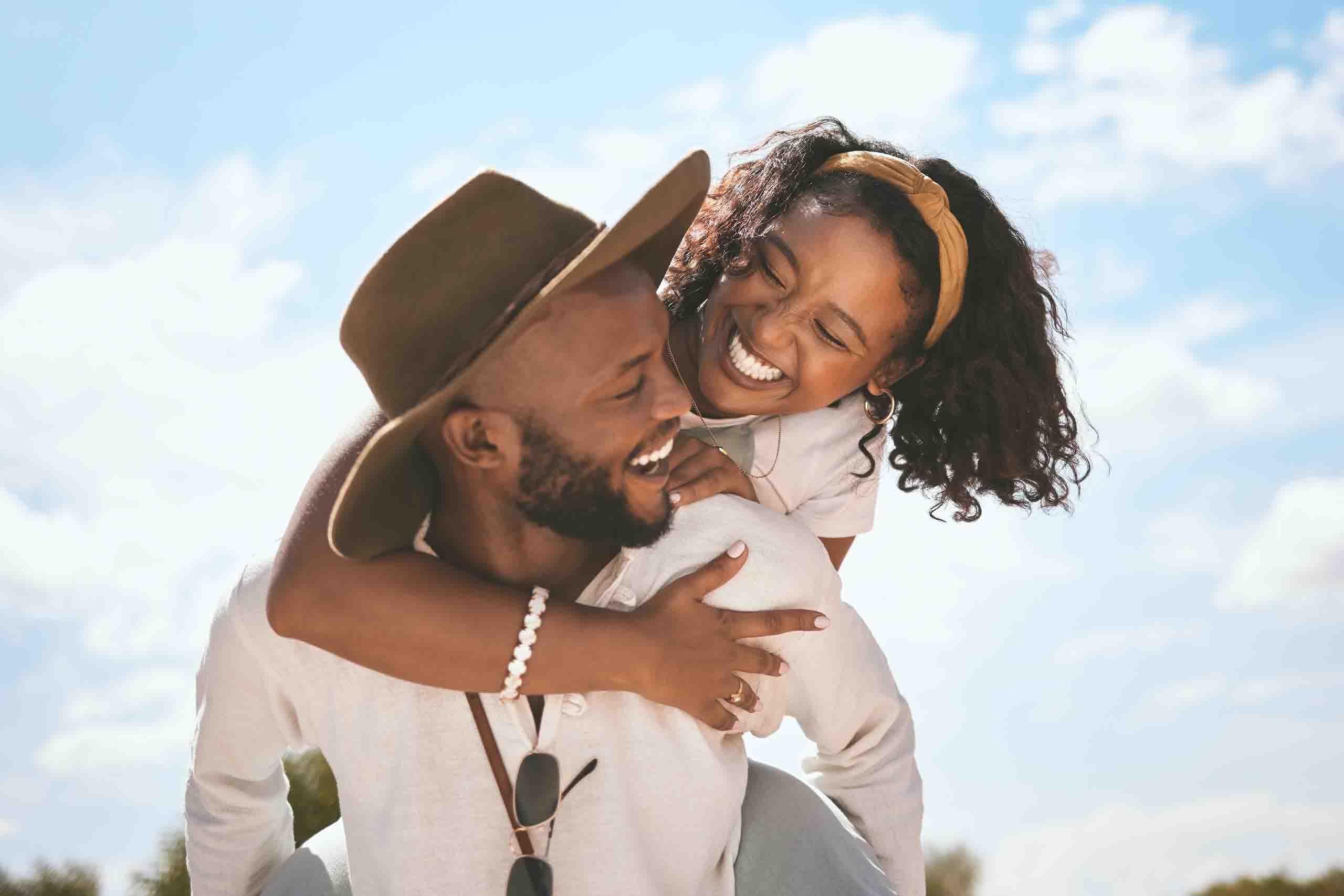 Couple enjoying outdoor fun with a piggyback ride under the blue sky, symbolizing health and well-being.