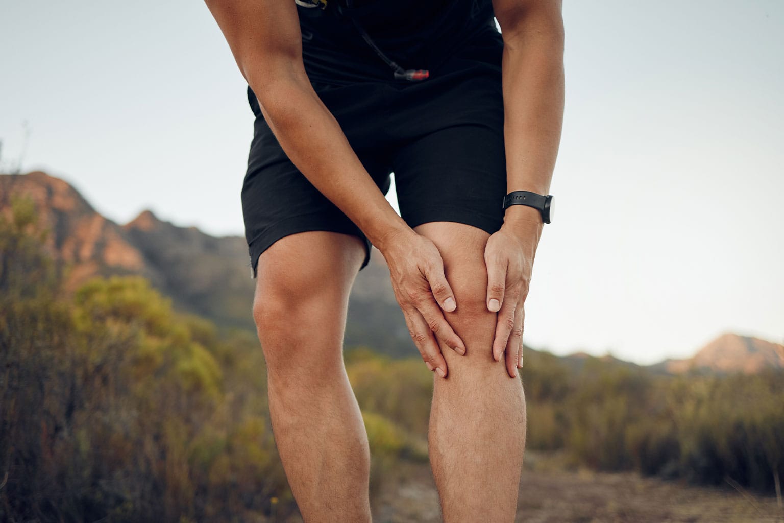 Man experiencing knee pain while hiking outdoors, highlighting the importance of seeking the right treatment for knee injuries.