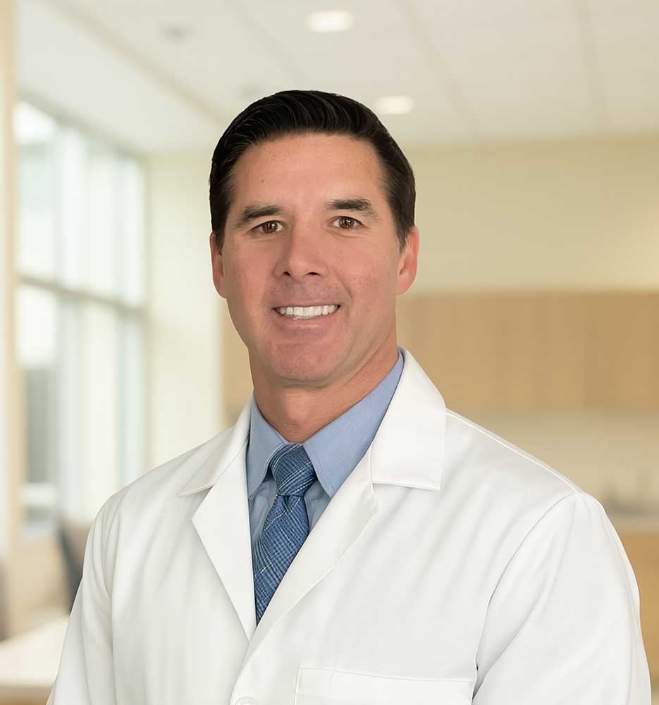 Smiling doctor in a white lab coat standing in a modern medical office.