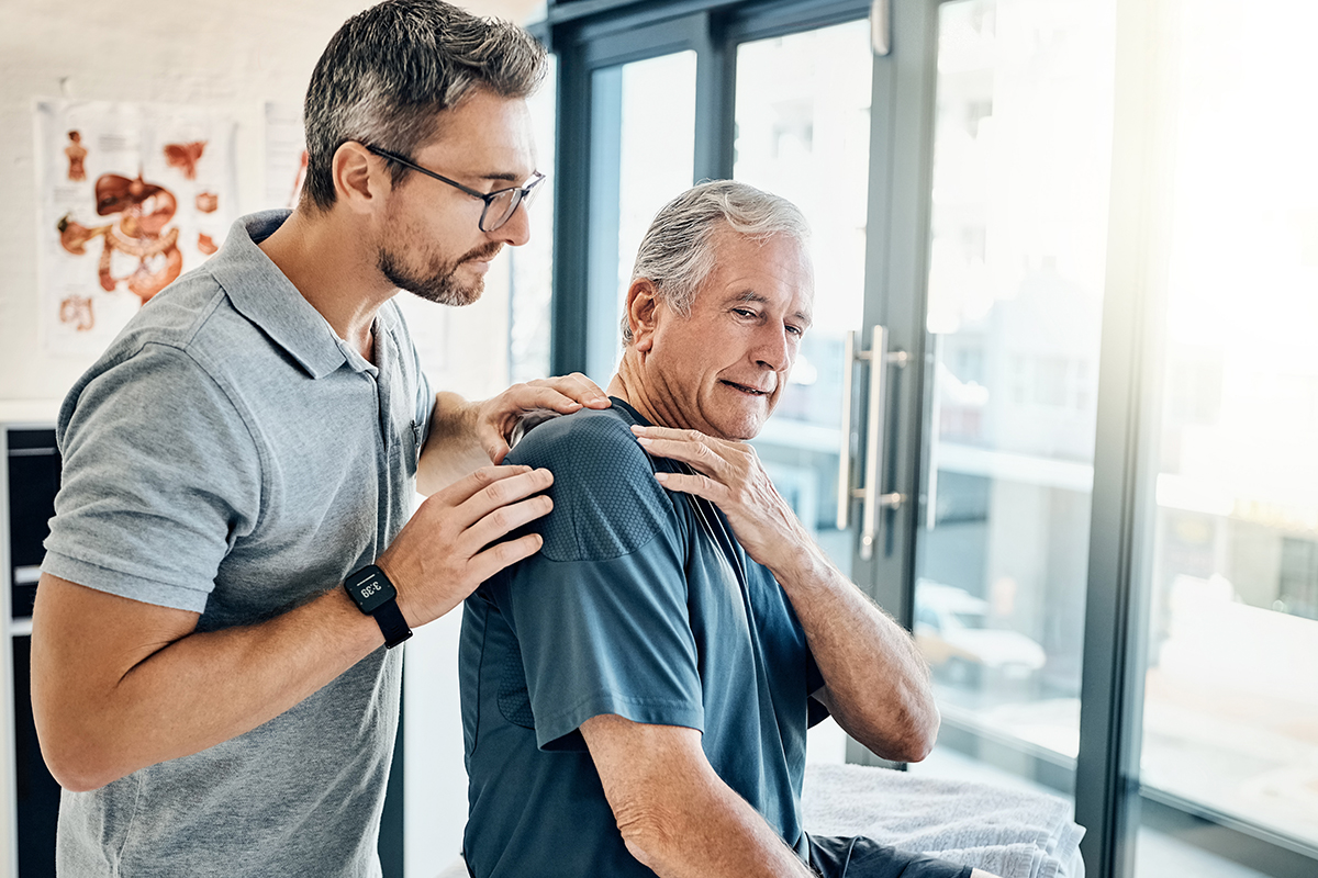 Physical therapist examining an older man's shoulder pain in a modern clinic setting